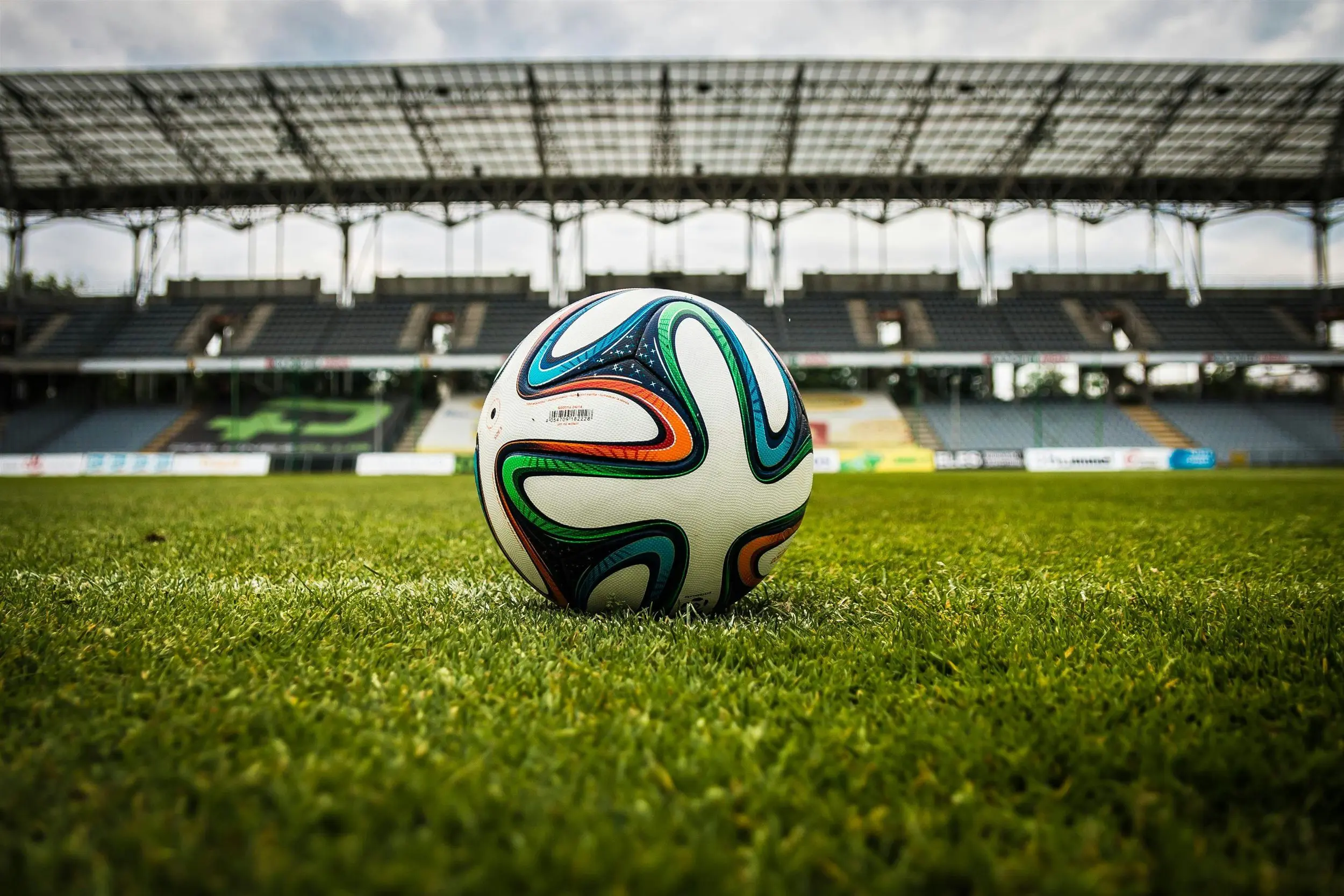 A soccer ball rests on the grass, positioned in front of an empty stadium.