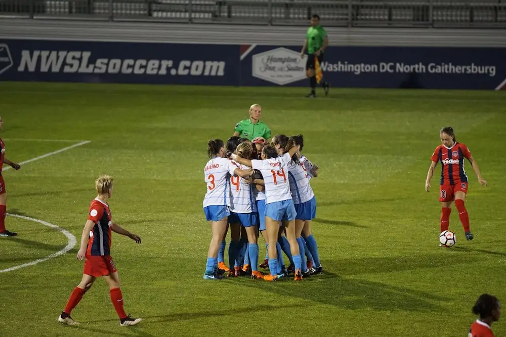 A women's soccer team gathers in a huddle on the field, focused and united as they prepare for their game.