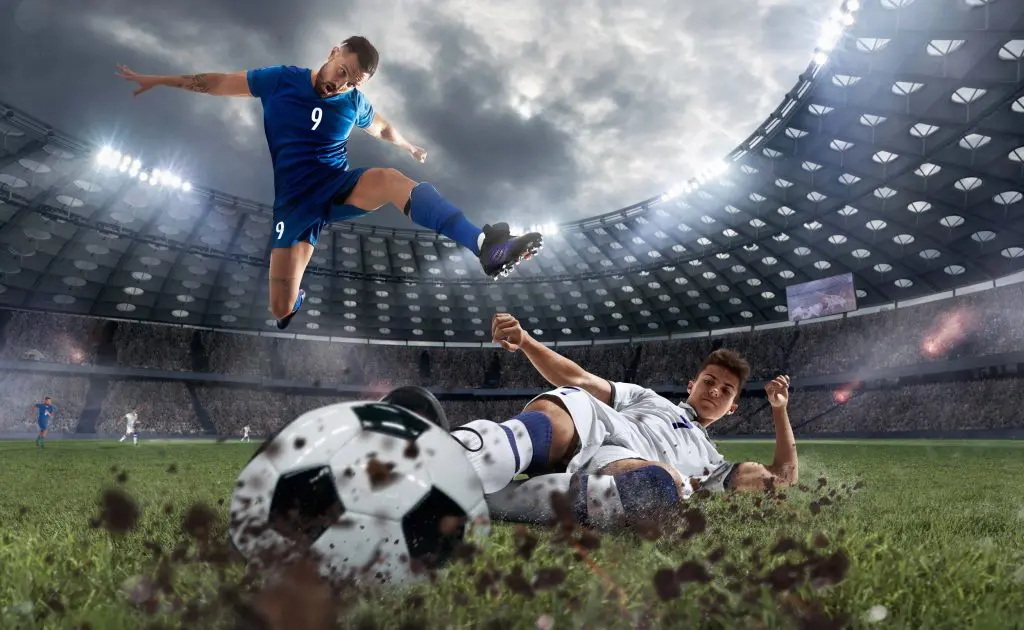 Two soccer players are skilfully kicking a ball high into the air during an intense match.