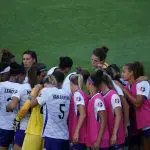 A group of high school soccer players huddle together, showcasing teamwork and camaraderie on the field.