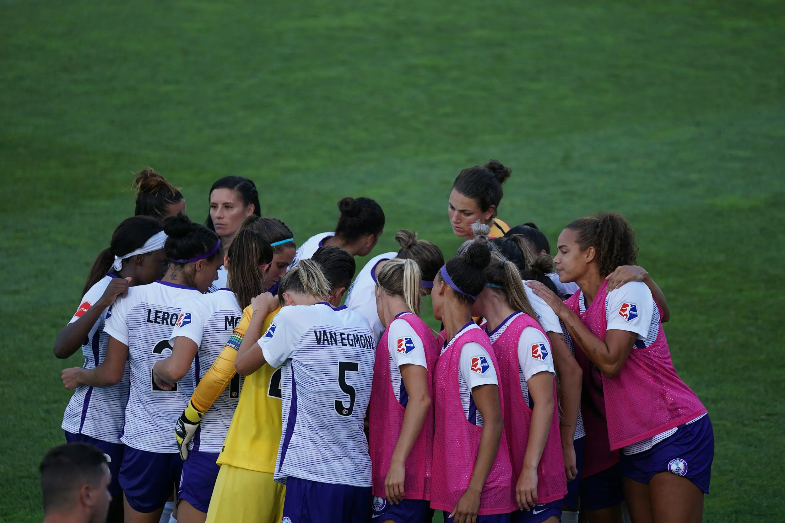 A group of women soccer players huddle together, showcasing teamwork and camaraderie on the field.