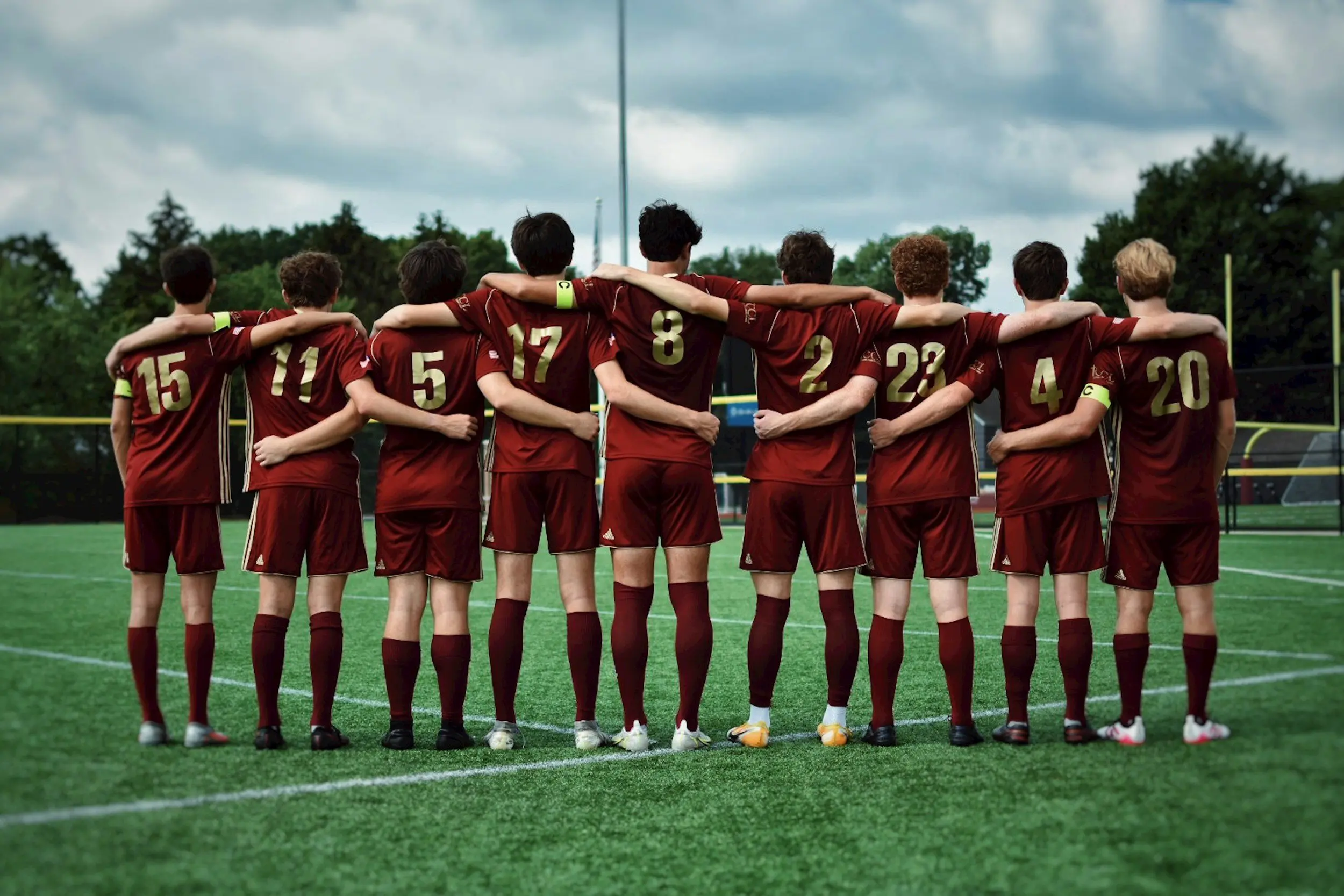 A group of boys in maroon uniforms stands together on a soccer field, ready for their game.