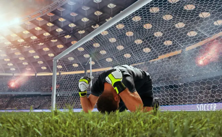 A soccer player kneels in front of the goal, preparing for a play or reflecting on the game.