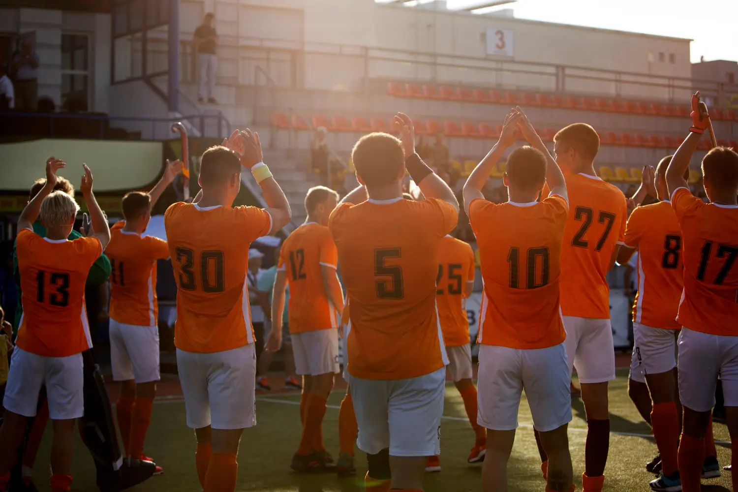 A team of soccer players dressed in orange shirts, actively participating in a game on a vibrant green field.