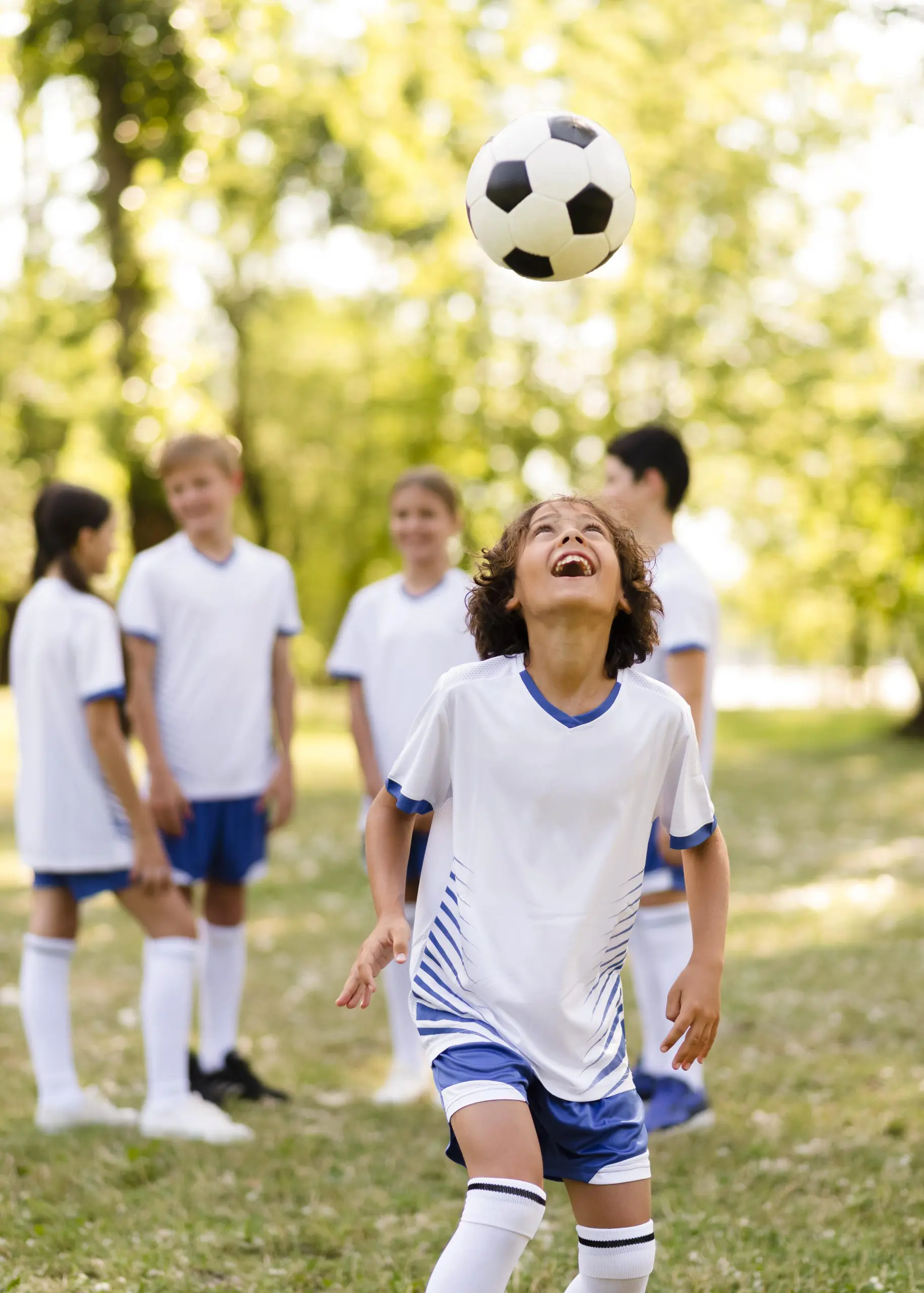 A young boy joyfully plays soccer with a group of children on a sunny field.