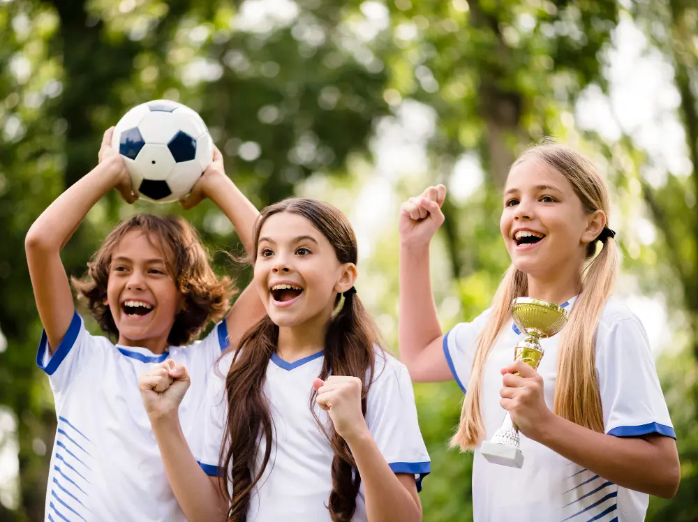 Three children proudly display a soccer ball and a trophy, celebrating their achievement in a sports event.