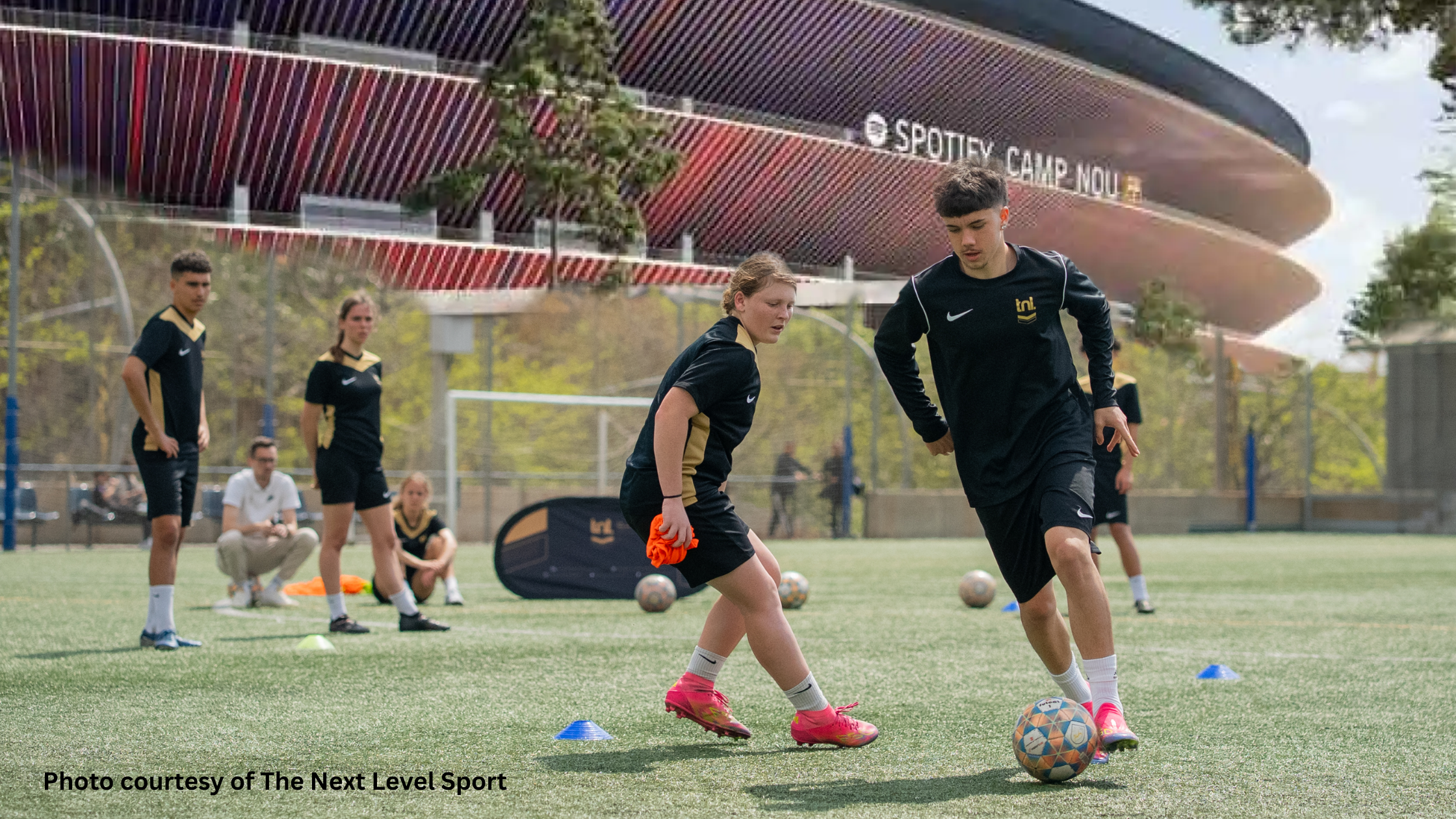 Youth players compete for the ball during a Next Level training session in Barcelona, with Spotify Camp Nou in the background. TNL Spanish Soccer Academy