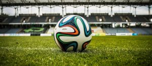 A soccer ball rests on the grass, positioned in front of an empty stadium.